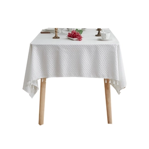 White herringbone textured tablecloth with tassels on a minimalist wooden dining table