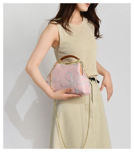 Close-up of floral embroidery on pink satin handbag with vintage wooden handle