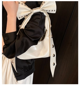 Detail of white patent leather bag with silver studs and a large bow design