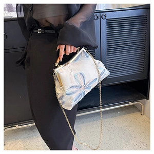 Detail of floral embroidery bag with wooden handle and gold chain strap held by model