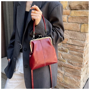 Detail of red kiss-lock handbag with white stitching and metallic hardware worn by a model