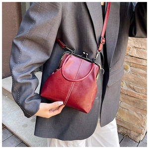 Retro red shell handbag with kiss-lock closure shown on a model in gray suit
