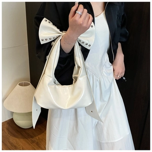 Detail of white patent leather hobo bag with oversized bow and silver rivets on a model