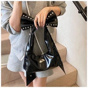 Detail of black patent leather bow handle with silver studs on a stylish crescent bag