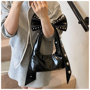 Detail of black patent leather shoulder bag with oversized bow and silver rivets