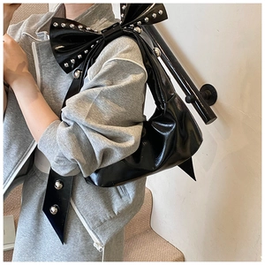 Detail of black glossy shoulder bag with a large bow and silver rivet embellishments