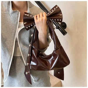 Close-up of vintage dark brown patent leather tote bag with rivets and bow shape