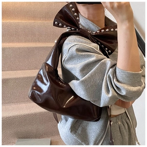 Detail of a dark brown glossy oil wax leather bag with studded bow handle and crescent shape