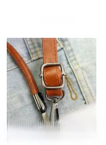 Detail view of brown faux leather shoulder strap with silver metal buckle on denim fabric