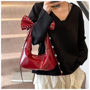 Detail of red patent leather shoulder bag with large bow and silver studs accents