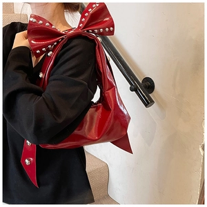 Detail of red patent leather shoulder bag featuring metal rivets and a large bow strap