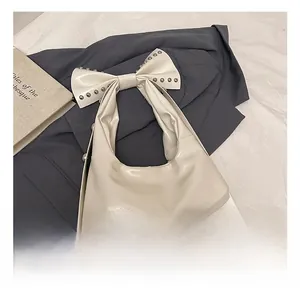 Close-up of a white patent leather shoulder bag with a large studded bow detail