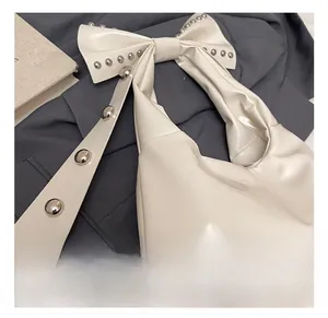 Close-up of white shoulder bag featuring silver rivets and a decorative oversized bow