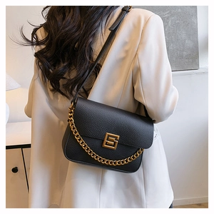 Detail of black lychee grain leather handbag with gold chain strap on a model