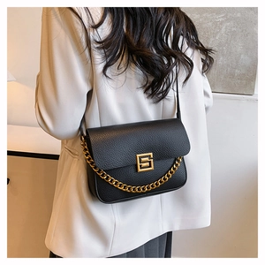 Detail of black pebbled leather bag featuring a gold chain and square metal buckle strap