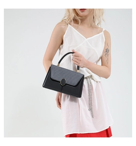 Detail of grey textured flap and gold buckle on a stylish black crossbody bag