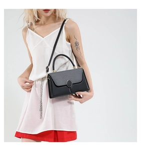 Detail of grey textured flap and golden oval lock on black leather crossbody bag