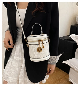 Detail of a vintage white cylinder bucket bag with gold relief pendant on a leather texture