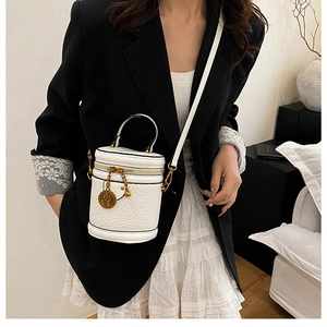Detail of white bucket bag with leather texture and engraved gold coin pendant