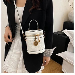Detail of white leather bucket bag with gold hardware and logo charm on a model