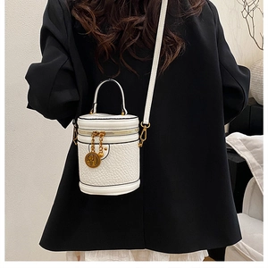 Detail of white embossed leather bucket bag with gold coin charm on black suit