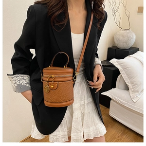 Brown vintage cylinder bag with crocodile texture worn crossbody by model in suit