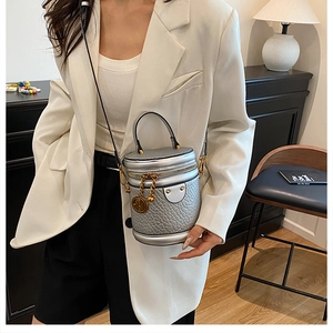 Detail of silver cylindrical bucket bag with embossed texture and gold metal charms