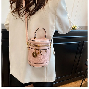 Close-up of pink litchi grain bucket bag featuring golden flower emblem and sleek strap