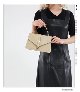 Detail of beige leather handbag with fine texture and golden buckle on black dress