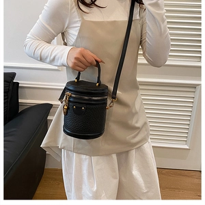 Detail of black textured bucket bag with gold zippers and adjustable shoulder strap