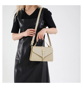 Detail of light gold woven crossbody bag featuring a golden lock and wide strap