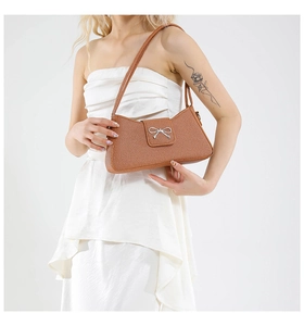 Brown woven baguette bag with silver bow clasp worn by model in white dress