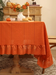 Detail of orange knitted tablecloth with elegant lace border on a rustic dining table