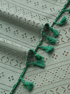 Dettaglio di tovaglia in pizzo grigio-verde con trama traforata e nappe verdi