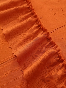 Macro view of bright orange lace fabric with floral hollow embroidery and wavy hem