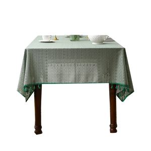Tovaglia in pizzo traforato verde scuro con motivo a rombi e frange su tavolo in legno