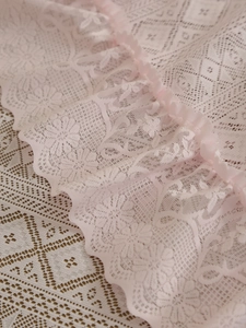Detail of pink vintage lace tablecloth featuring hollow floral patterns and wavy edges