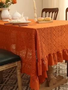 Detail of warm orange lace tablecloth with geometric hollow patterns and ruffle edges