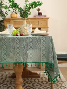 Sage green hollow lace tablecloth with geometric patterns and fringe tassels on wood table