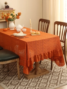 Detail of orange crochet lace tablecloth with intricate diamond patterns and ruffled edges