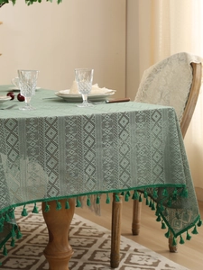 Close-up of dark green hollow lace tablecloth with geometric patterns and fringe tassels