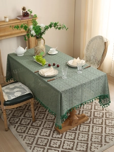 Detail of green lace tablecloth featuring hollow crochet pattern and tassel edges