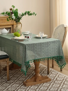 Detail of dark green hollow lace tablecloth with fringe edge on a vintage wooden table