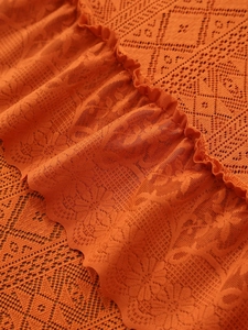 Close-up of burnt orange lace tablecloth showing hollow floral and diamond knit patterns