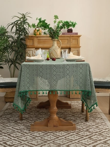 Detail of green hollow lace tablecloth with geometric patterns and fringe on wood table