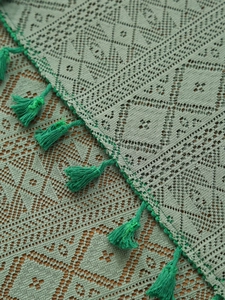 Detailed macro view of gray-green hollow lace tablecloth with handmade fringe and tassel edge