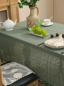 Detailed close-up of dark green crochet lace tablecloth with tassels and geometric patterns