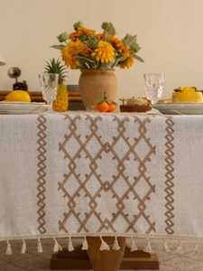 Close-up of beige linen tablecloth with brown geometric embroidery and elegant tassels
