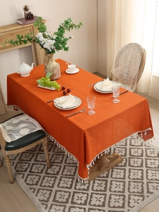 Detailed close-up of orange hollow lace tablecloth with white fringe on a rectangular table