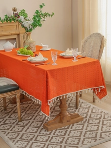 Close-up of bright orange hollow lace tablecloth with white tassel details and floral pattern